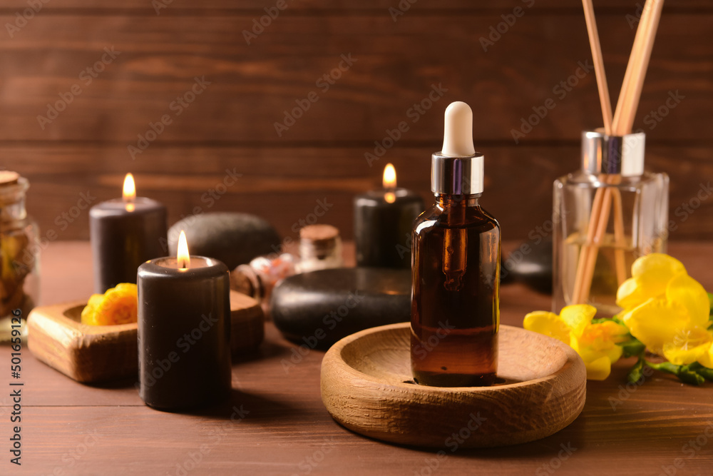 Bottle of essential oil and burning candles on wooden background
