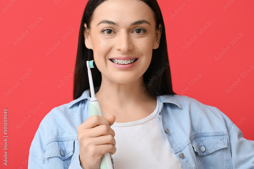 Beautiful woman with dental braces and electric toothbrush on red background Beautiful woman with dental braces and electric toothbrush on red background