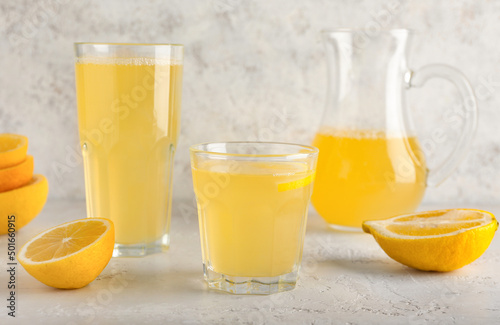 Glasses with fresh lemon juice on light background