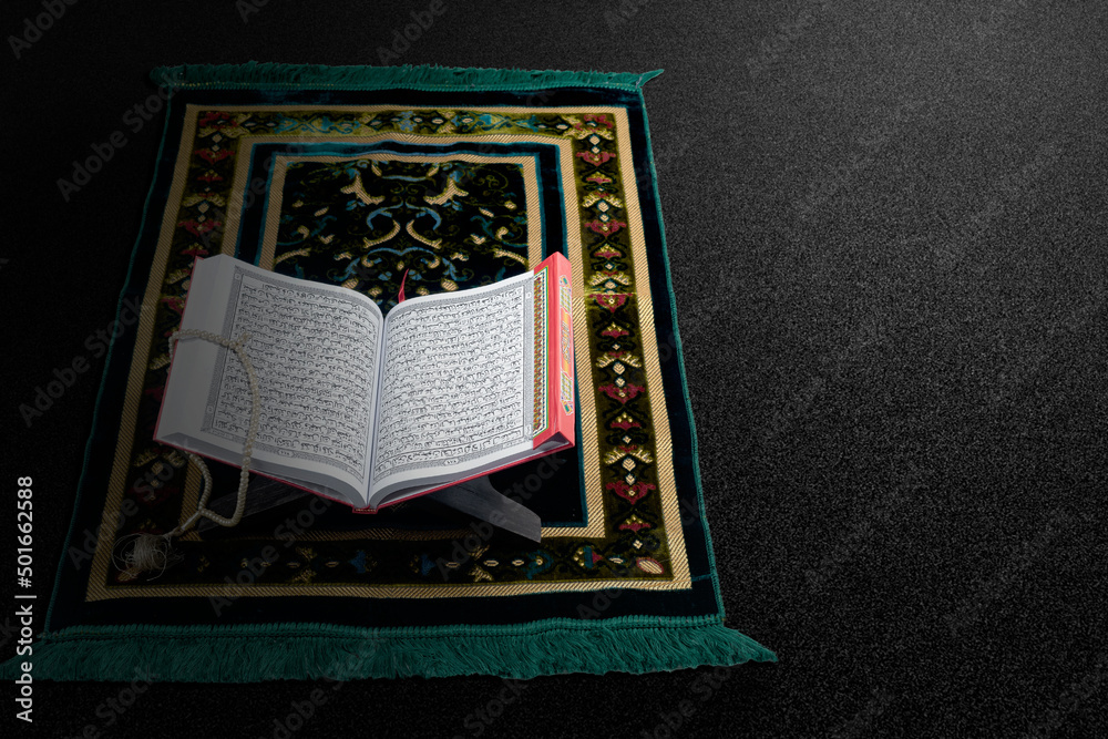 Quran open on a wooden placemat with prayer beads on a prayer rug Quran open on a wooden placemat with prayer beads on a prayer rug