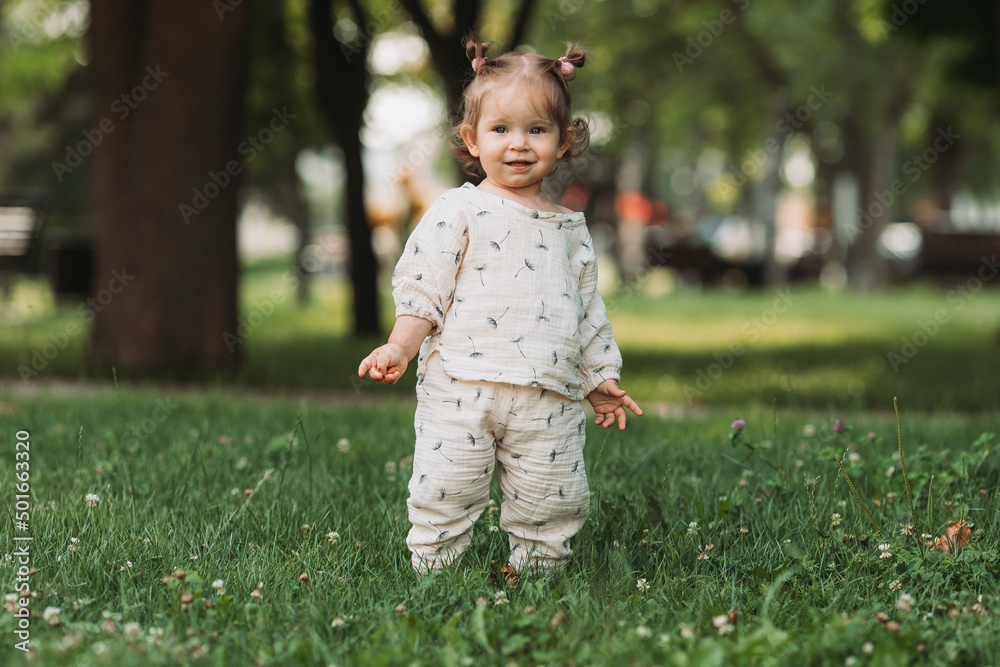 cute little smiling girl with a funny hairstyle hides behind trees and runs and plays in the park cute little smiling girl with a funny hairstyle hides behind trees and runs and plays in the park