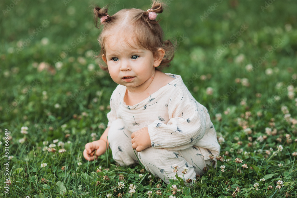 cute little girl with a funny hairstyle is sitting on a blooming green lawn in the park. lifestyle cute little girl with a funny hairstyle is sitting on a blooming green lawn in the park. lifestyle