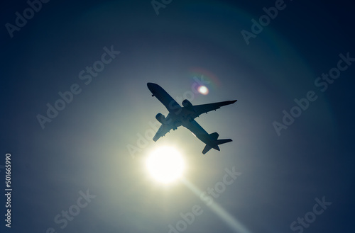dark airplane silhouette on the sun, blue sky background with reflections.