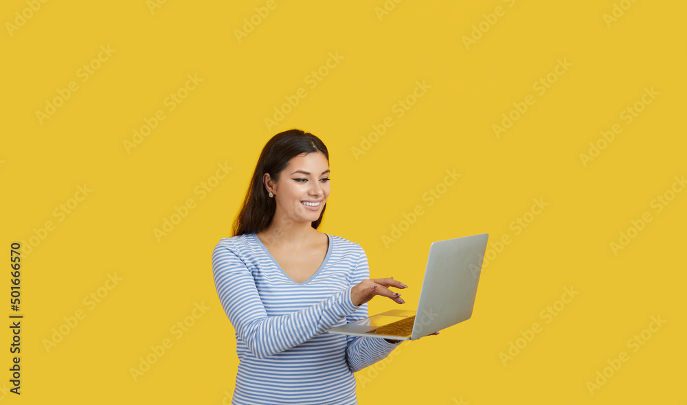 Naklejka premium Happy woman with laptop making presentation, working, shopping online or corresponding with friends. Smiling caucasian brunette woman with laptop isolated on vivid yellow background. Online concept.