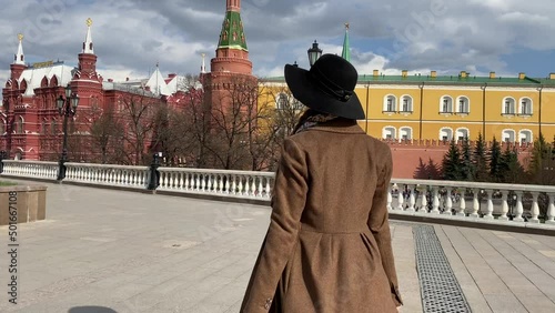 Young beautiful lady elegance madame in hat and coat walking on Red Square  near Historical Museum, Kremlin, Alexander Garden and Okhotny Ryad. Spring, blooming flowers. Center of Moscow, Russia. photo