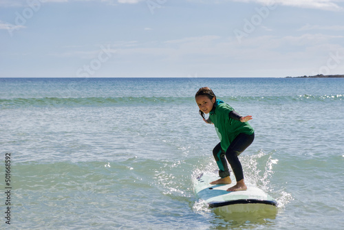 Surf school. 6-year-old girl surfs a small wave on her board before reaching the beach.
