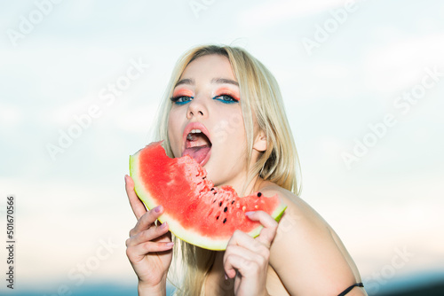 Sexy girl eating a watermelon. Blonde young woman model with bright makeup and red lips. Summer sexy watermelon. Sensual young woman lick watermelon with sexy tongue. photo