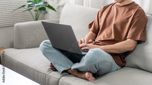Technology Concept The male who is wearing casual clothes sitting on the sofa, resting his notebook on his lap and doing his work