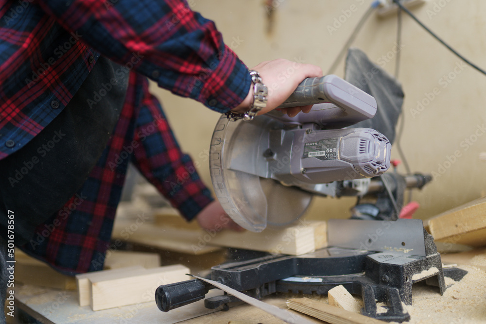 carpenter in a plaid shirt sawing wood on the machine