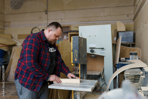 carpenter in a plaid shirt sawing wood on the machine