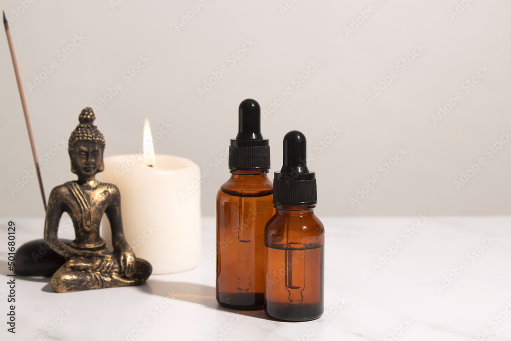 Spa treatment bottle of natural organic oil essence serum collagen. Aromatherapy and beauty concept. Aroma bottle with essential oils and Buddha on white background. Copy space for text. Spa treatment bottle of natural organic oil essence serum collagen. Aromatherapy and beauty concept. Aroma bottle with essential oils and Buddha on white background. Copy space for text.