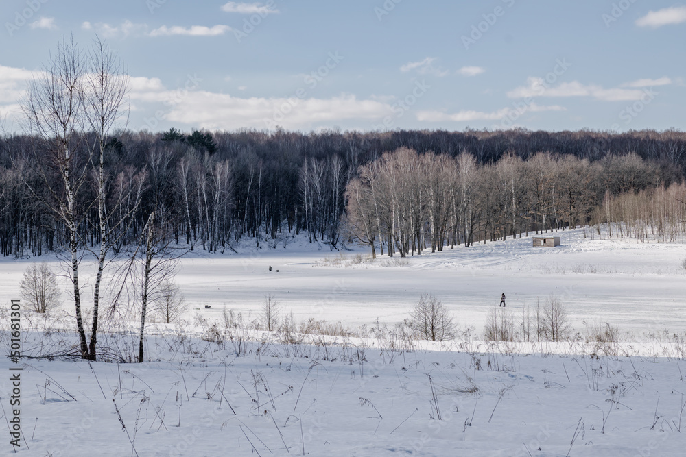 Winter landscape of frozen and snow-covered lake with male figures surrounded by forest against blue cloudy sky. Winter landscape of frozen and snow-covered lake with male figures surrounded by forest against blue cloudy sky.