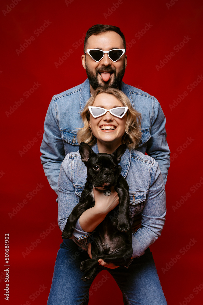 Obraz premium happy couple wearing sunglasses holding a french dog. happy family concept.