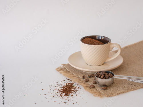 Fototapeta Naklejka Na Ścianę i Meble -  A coffee cup with a saucer on a canvas napkin, grains and ground coffee are scattered on the table and a serving spoon. Space for copy