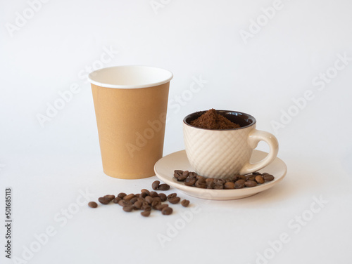 Ground coffee in a cup with a saucer, coffee beans and a disposable paper cup with space for text.