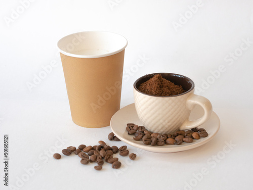 Ground coffee in a cup with a saucer, coffee beans and a disposable paper cup with space for text