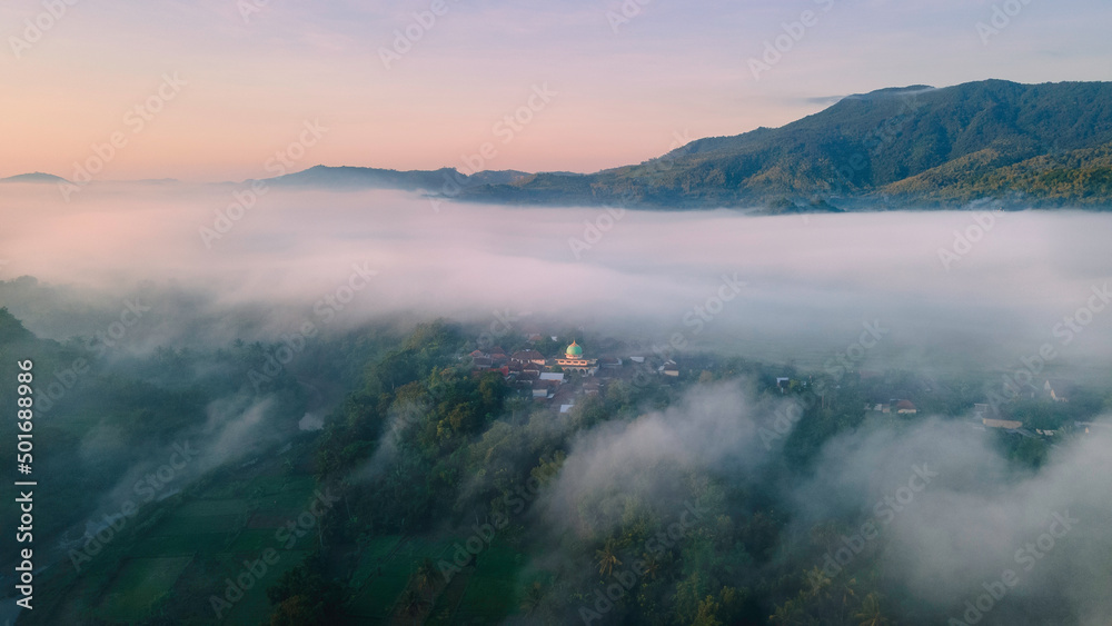 Aerial view, a village covered in a sea of ​​mist in the morning with a view of the dome of the mosque