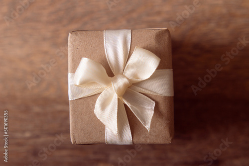 Gift box wrapped with craft paper and bow on neutral background