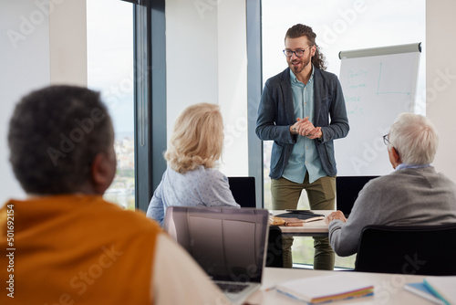 Young educator teaching a multicultural group of senior students in the classroom.