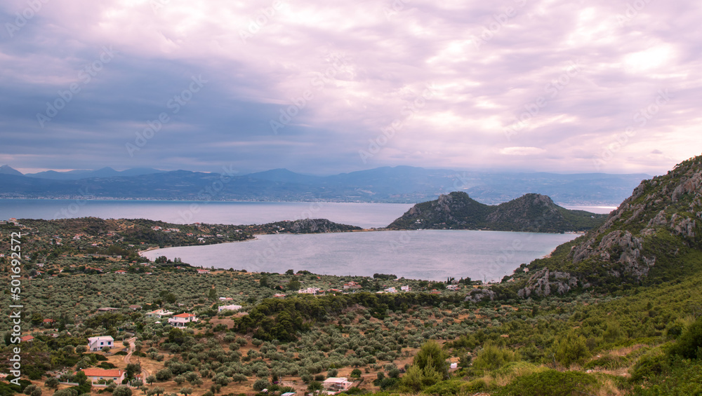 Amazing landscape, foothill village, high mountains, calm sea, lilac dramatic sky with thick white clouds, Greece 