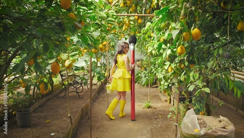Fashion model works, creative art photo shoot process. fantasy woman artist turned away, holding large magic brush in hand. Girl poses photographer. Yellow dress. Natural garden landscape lemon trees