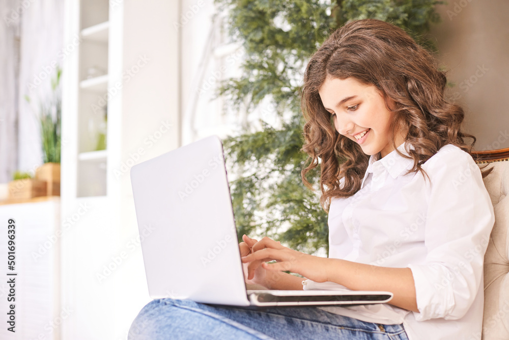 Female teenager laptop on sofa. Glad teen student using netbook for studies. Sitting on couch at home. School online lessons. Browing news. Optimist university girl portrait. Notebook homework Female teenager laptop on sofa. Glad teen student using netbook for studies. Sitting on couch at home. School online lessons. Browing news. Optimist university girl portrait. Notebook homework