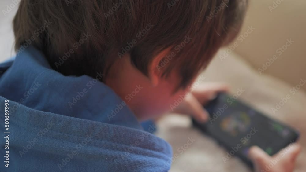 Child Playing Games In Phone at Home Lying on Couch. Boy Playing Video Game on Mobile Phone. Preschooler Plays Video Game Smartphone on Sofa. Kid Using Phone for Gaming Online Education Social Media. Child Playing Games In Phone at Home Lying on Couch. Boy Playing Video Game on Mobile Phone. Preschooler Plays Video Game Smartphone on Sofa. Kid Using Phone for Gaming Online Education Social Media.