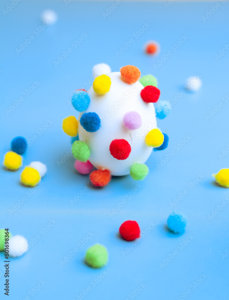 Egg with colorful pom-poms and scattered pom-poms, side view, selective focus