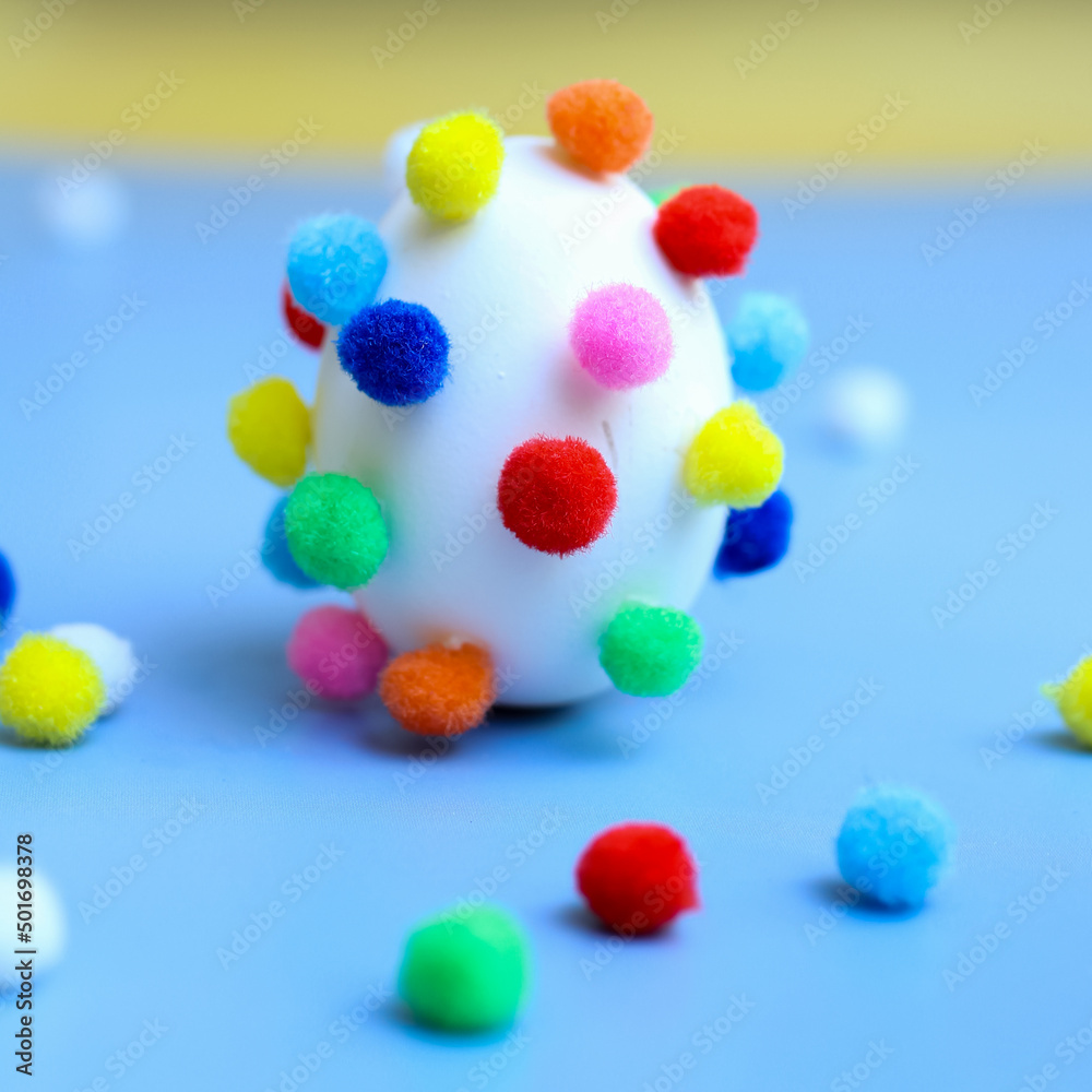 Egg with colorful pom-poms and scattered pom-poms, side view, selective focus Egg with colorful pom-poms and scattered pom-poms, side view, selective focus