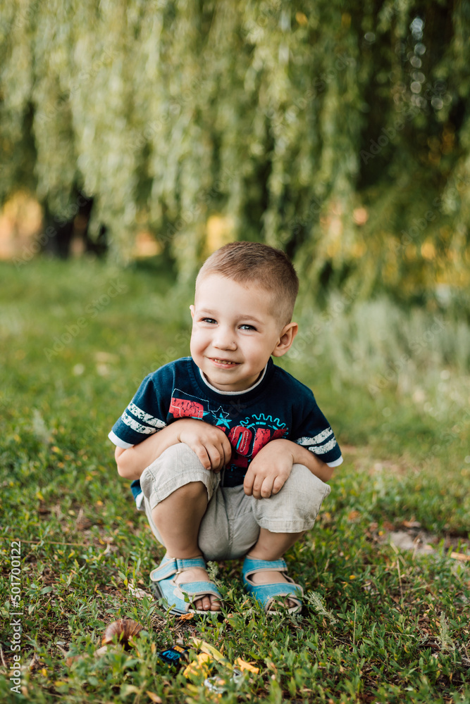 Little boy sits in the grass and smiles sweetly Little boy sits in the grass and smiles sweetly