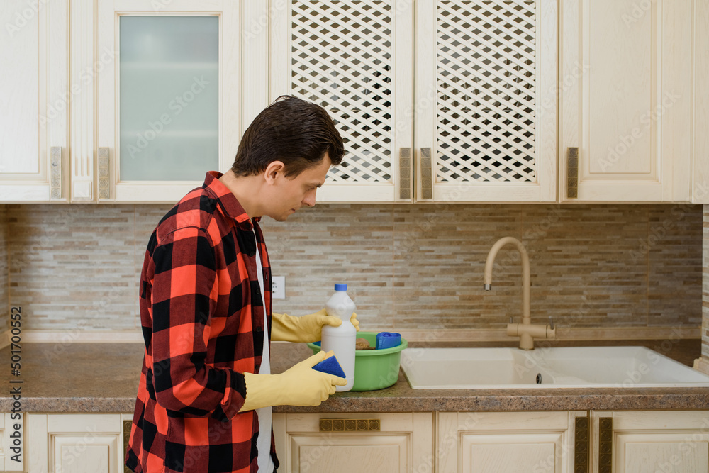 young man in a red checkered shirt holding cleaning products and prepare for cleaning the kitchen. young man in a red checkered shirt holding cleaning products and prepare for cleaning the kitchen.