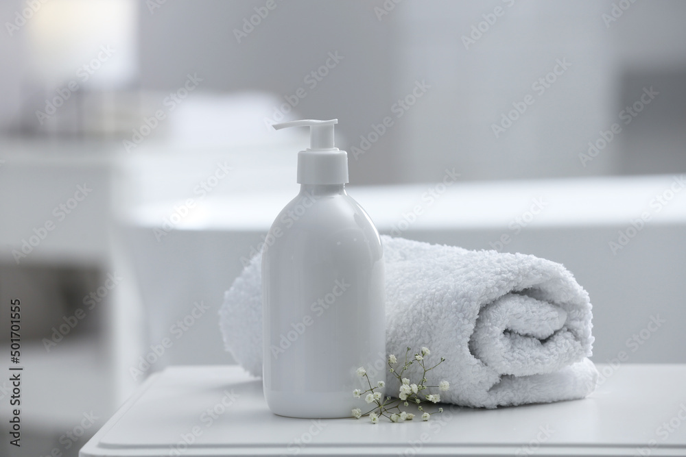 Bottle of bubble bath, towel and flowers on white table in bathroom Bottle of bubble bath, towel and flowers on white table in bathroom