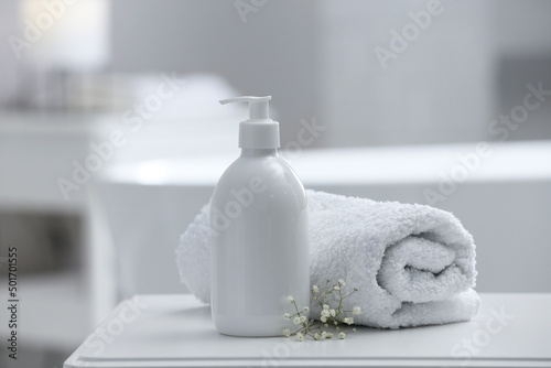 Bottle of bubble bath, towel and flowers on white table in bathroom