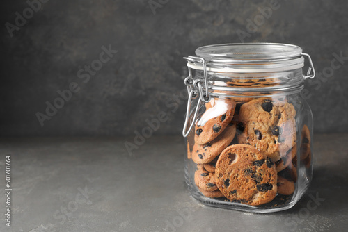 Fotografering Delicious chocolate chip cookies in glass jar on grey table, space for text