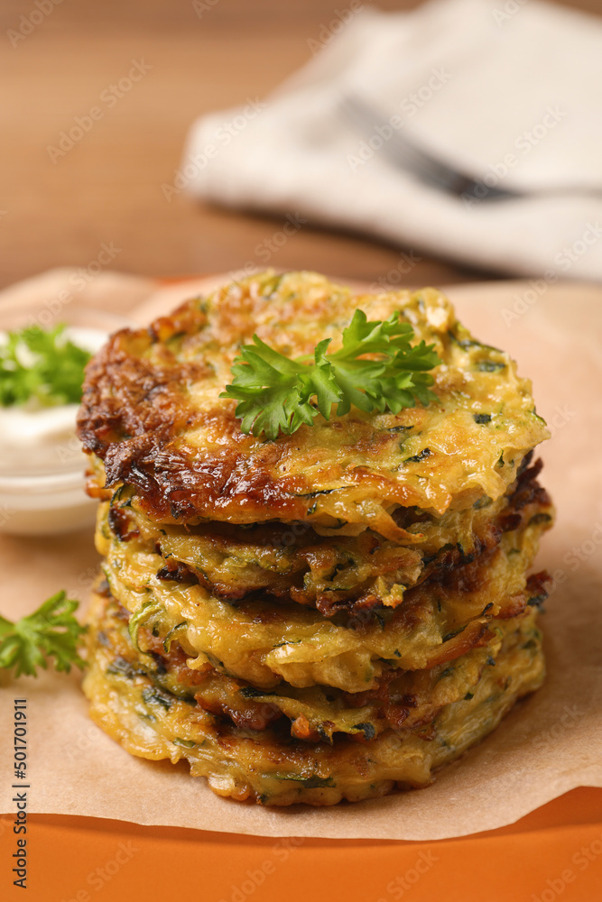 Delicious zucchini pancakes and bowl with sour cream on table, closeup Delicious zucchini pancakes and bowl with sour cream on table, closeup