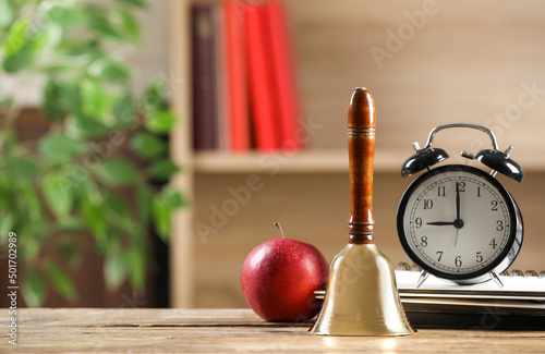 Golden school bell, apple, alarm clock and notebooks on wooden table in classroom, space for text photo