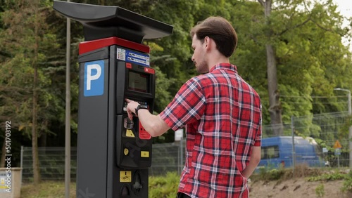 Young man use parking meter to pay for car parking photo