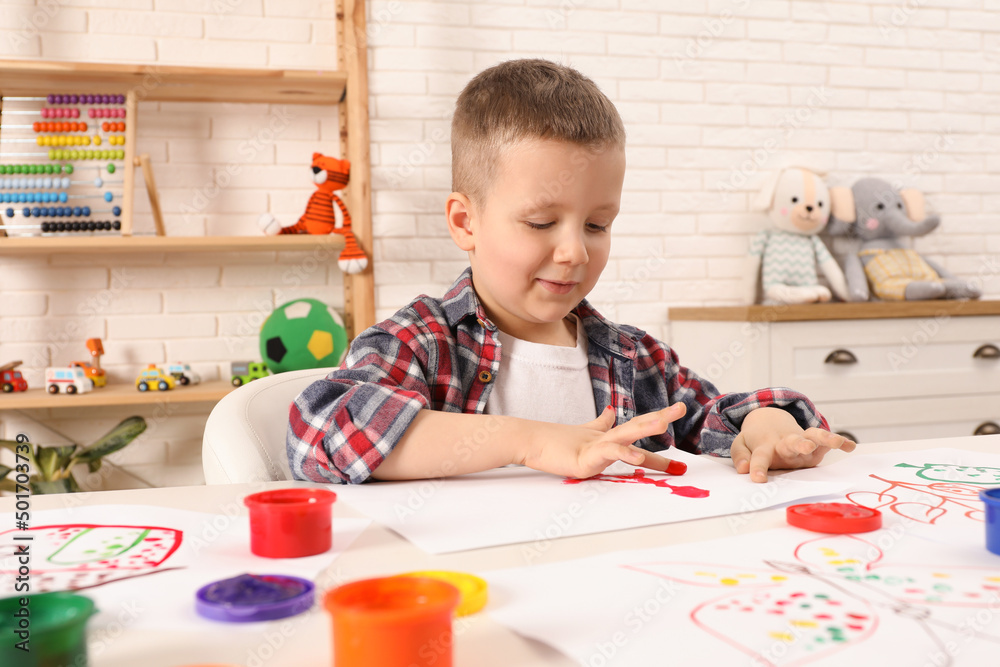Little boy painting with finger at white table indoors Little boy painting with finger at white table indoors