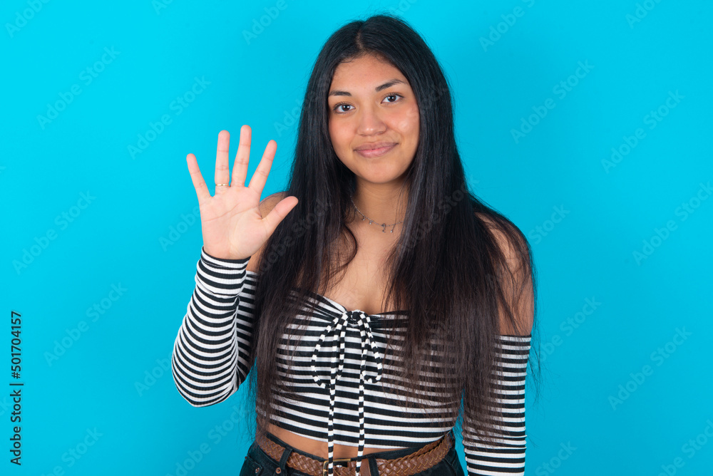 young latin woman wearing striped T-shirt over blue background showing and pointing up with fingers number five while smiling confident and happy. young latin woman wearing striped T-shirt over blue background showing and pointing up with fingers number five while smiling confident and happy.