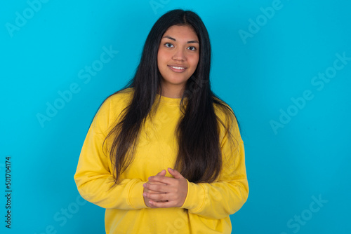 Business Concept - Portrait of young latin woman wearing yellow sweater over blue background holding hands with confident face.