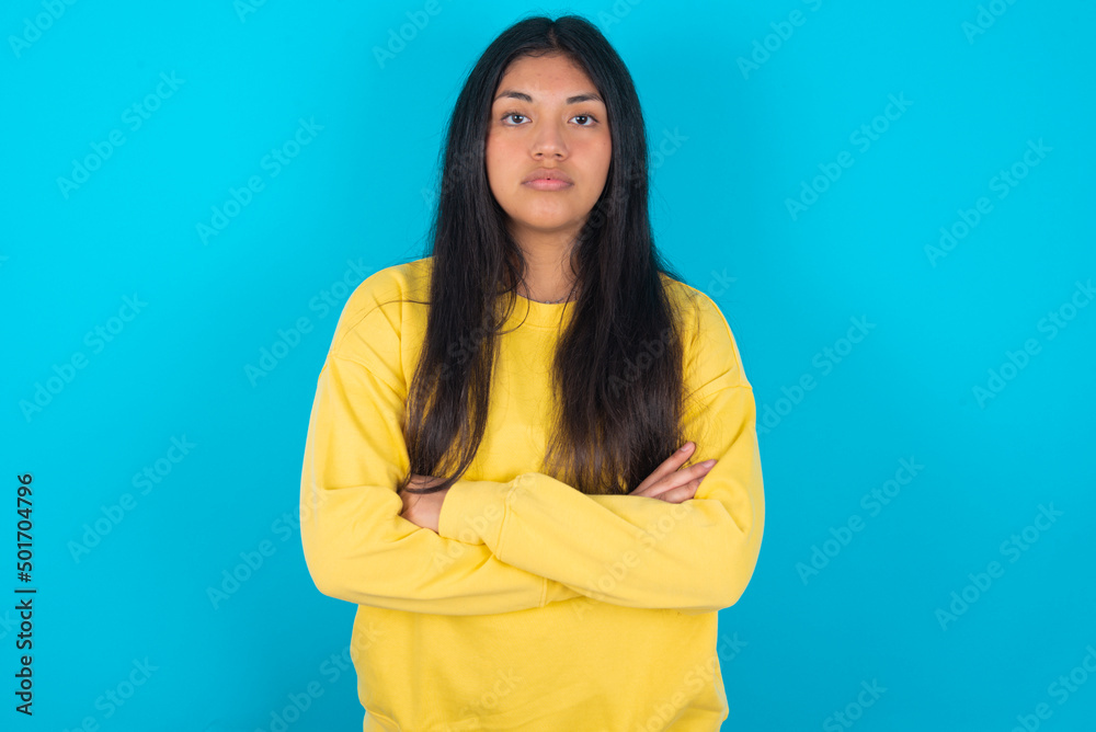 Picture of angry young latin woman wearing yellow sweater over blue background looking camera. Picture of angry young latin woman wearing yellow sweater over blue background looking camera.