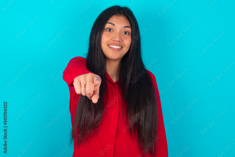 Excited positive young latin woman wearing red shirt over blue background points index finger directly at you, sees something very funny. Wow, amazing Excited positive young latin woman wearing red shirt over blue background points index finger directly at you, sees something very funny. Wow, amazing