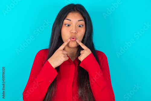 Photography young latin woman wearing red shirt over blue background crosses eyes and makes