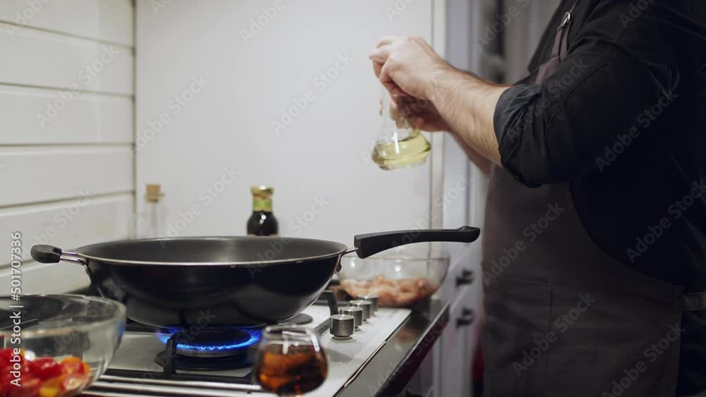 Roasting fresh vegetables in a wok. Male cook pouring oil into a frying pan Roasting fresh vegetables in a wok. Male cook pouring oil into a frying pan