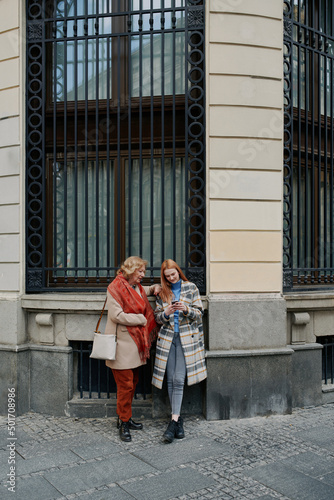 A grandmother and her grandchild standing on the street and reading messages on the phone. © chika_milan