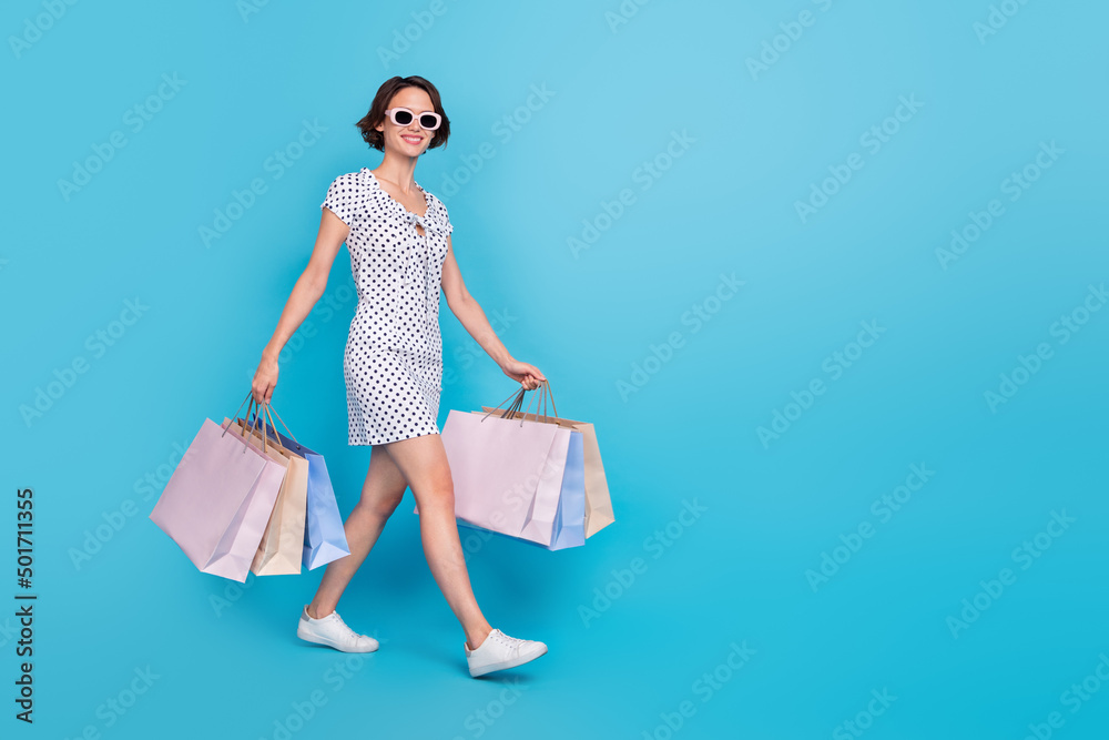 Full size profile portrait of pretty positive girl hold packages walking isolated on blue color background