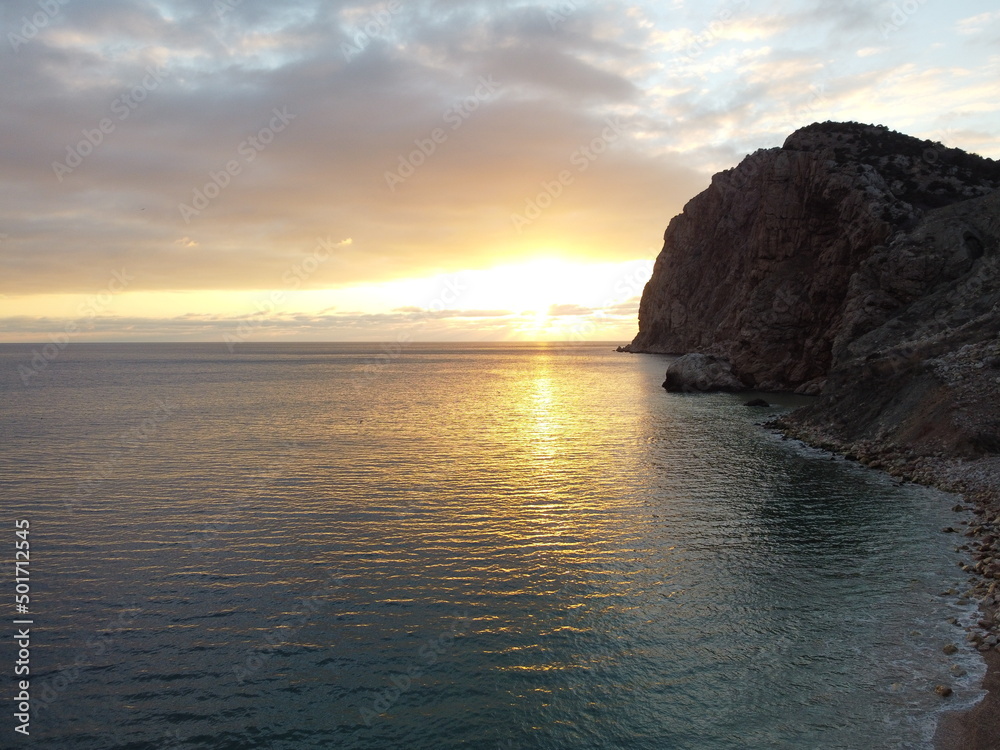 Aerial panoramic view of beautiful sunset above calm azure sea and volcanic rocky shores. Sun glare, small waves on the water surface. Horizon. Nobody. No people. Never-ending beauty of nature