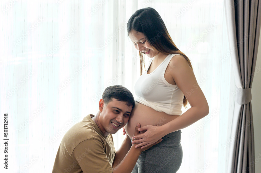 Young pregnant woman with husband embracing and expecting a baby at home Young pregnant woman with husband embracing and expecting a baby at home