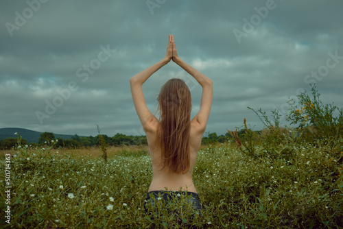 young woman doing yoga exercises on a field with many white flowers