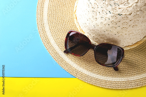 Sunglasses lie on the brim of a wicker hat.